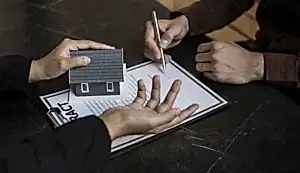 Bir kişinin elinde maket ev tutarken, diğer bir kişinin sözleşme imzaladığı, gayrimenkul hukuku danışmanlığını ve mülk alım satım süreçlerini temsil eden görsel.