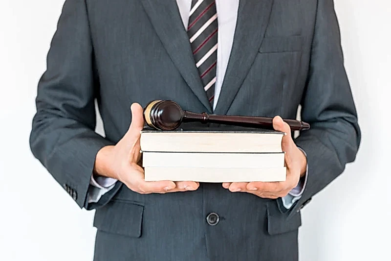 Takım elbiseli avukat, elinde hukuk kitapları ve yargı tokmağı ile – profesyonel hukuk danışmanlığı ve dava süreci.