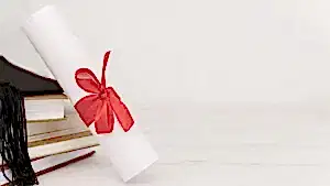 Beyaz bir arka plan üzerinde, kırmızı kurdeleyle bağlanmış bir diploma rulosu, yanında istiflenmiş kitaplar ve bir mezuniyet kepiyle akademik başarıyı temsil eden görsel.