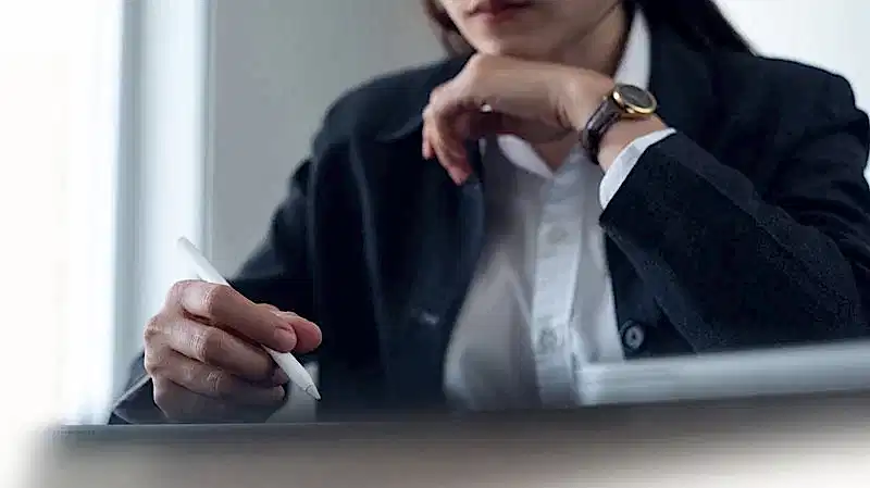 Profesyonel bir takım elbise giymiş bir hukukçunun veya danışmanın elinde stylus kalemle belge veya tableti incelediği, derinlemesine düşünce anını gösteren yakın çekim.