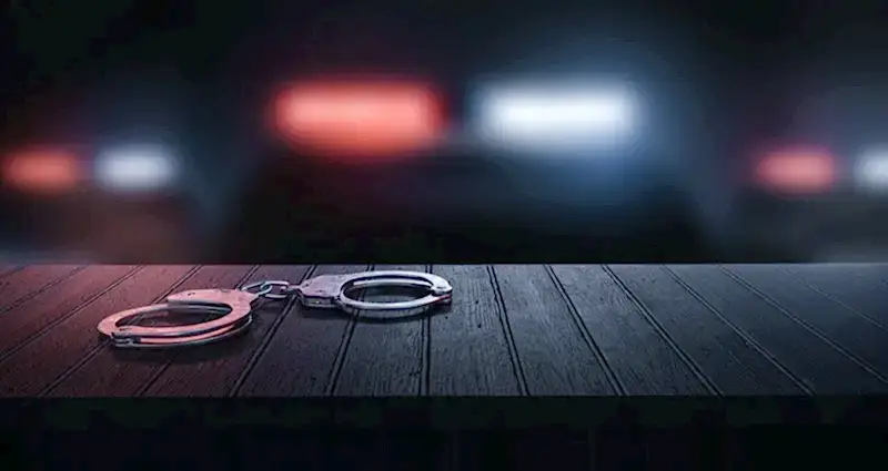 Loş ortamda masada duran kelepçe ve polis ışıkları – suç duyurusu süreci, şikayet dilekçesi ve hukuki başvuru yolları.